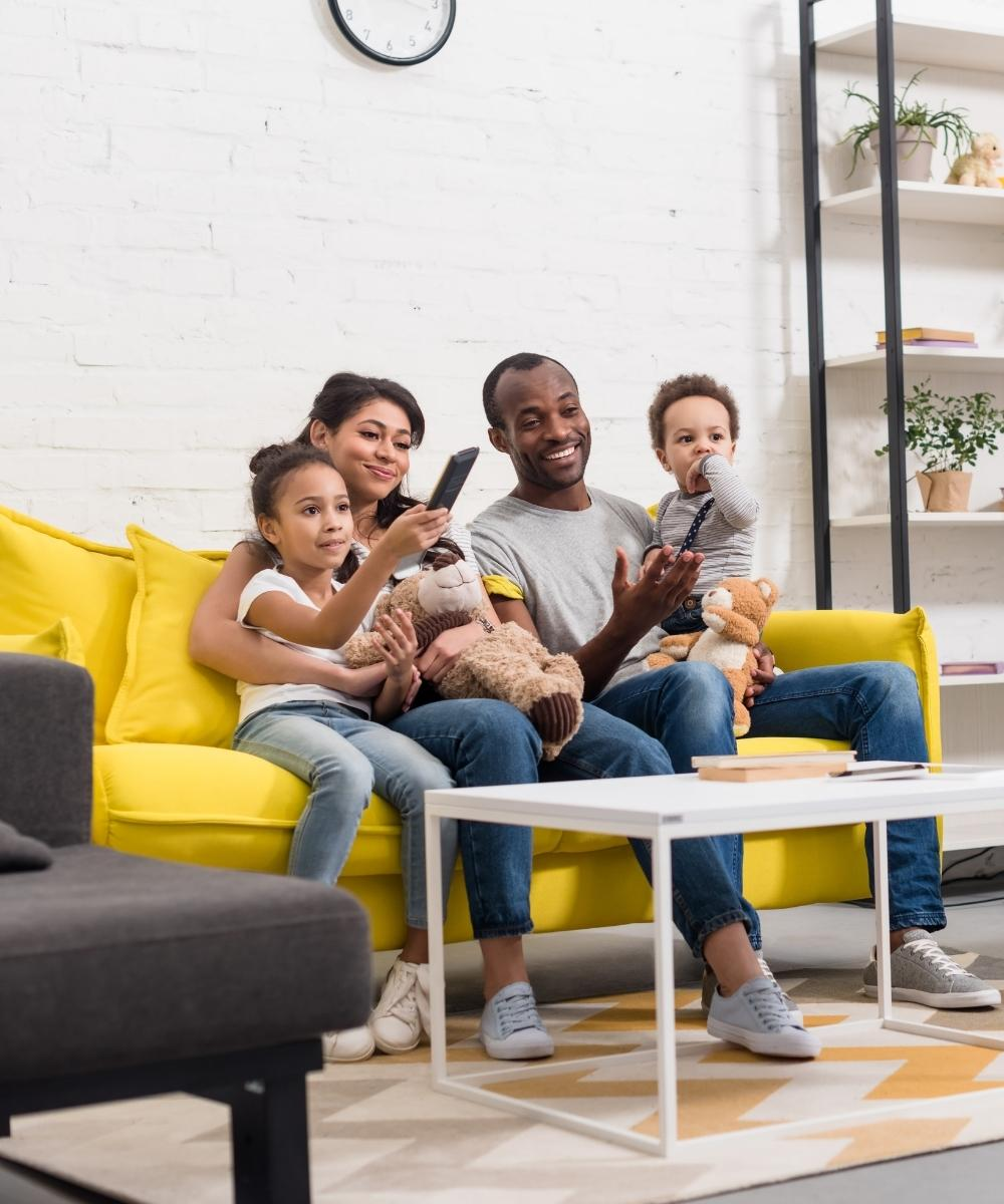 family of four sitting with two small kids on yellow sofa