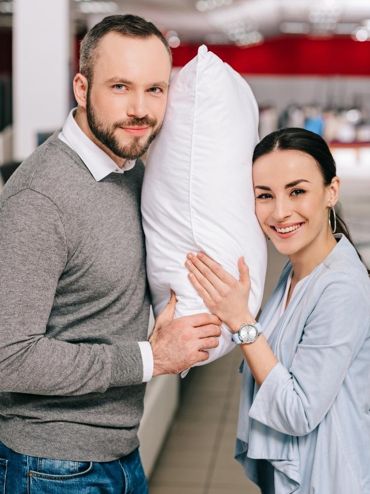 man and woman smiling and both holding a pillow
