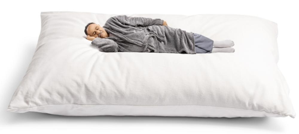 man in gray robe sleeping on a giant, comically large pillow