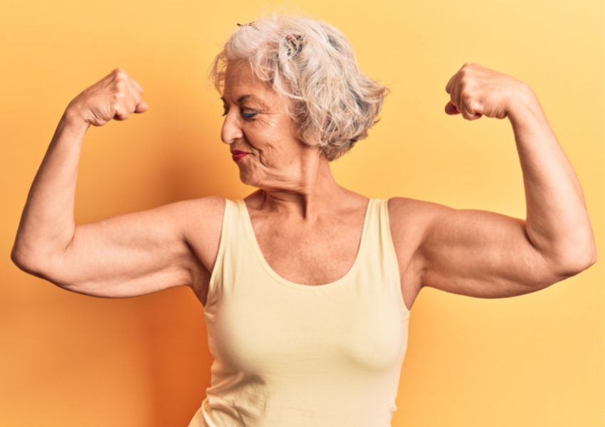 smiling woman with gray hair in yellow shirt flexing her arm muscles
