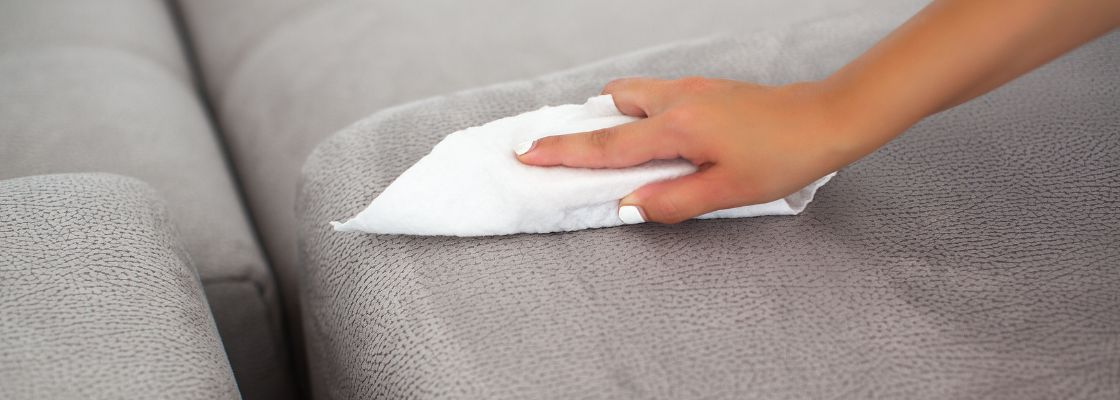 woman's hand with white nail polish cleaning gray leather upholstery with a cloth