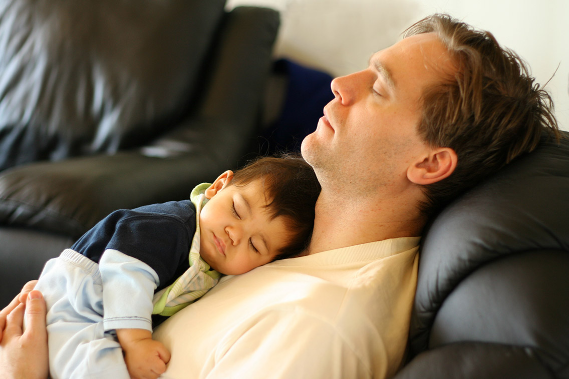 man sleeping on recliner with infant