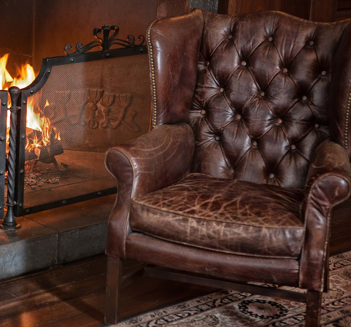 worn brown leather chair by fireplace