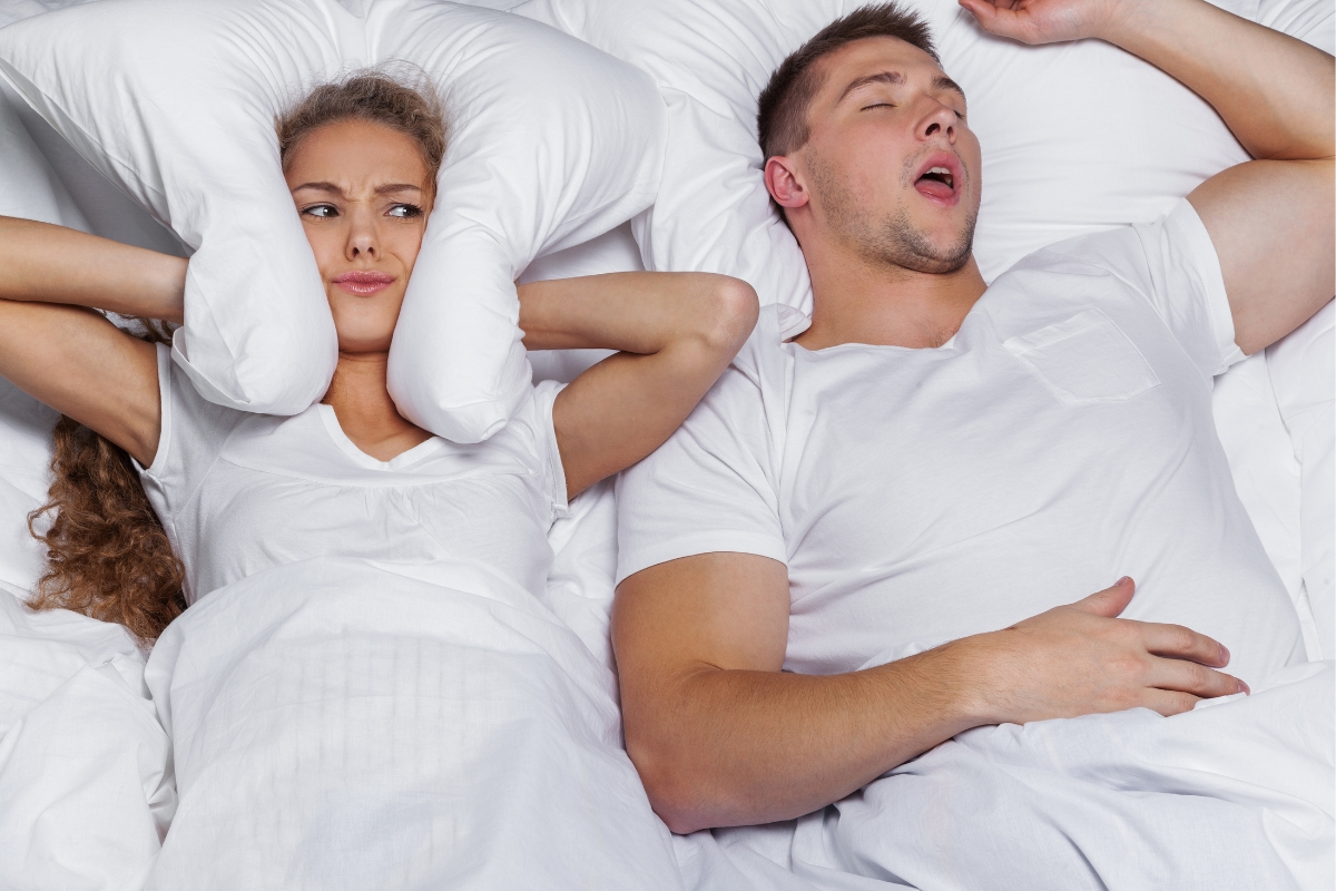 woman-covering-ears-in-bed-while-man-snores-asleep