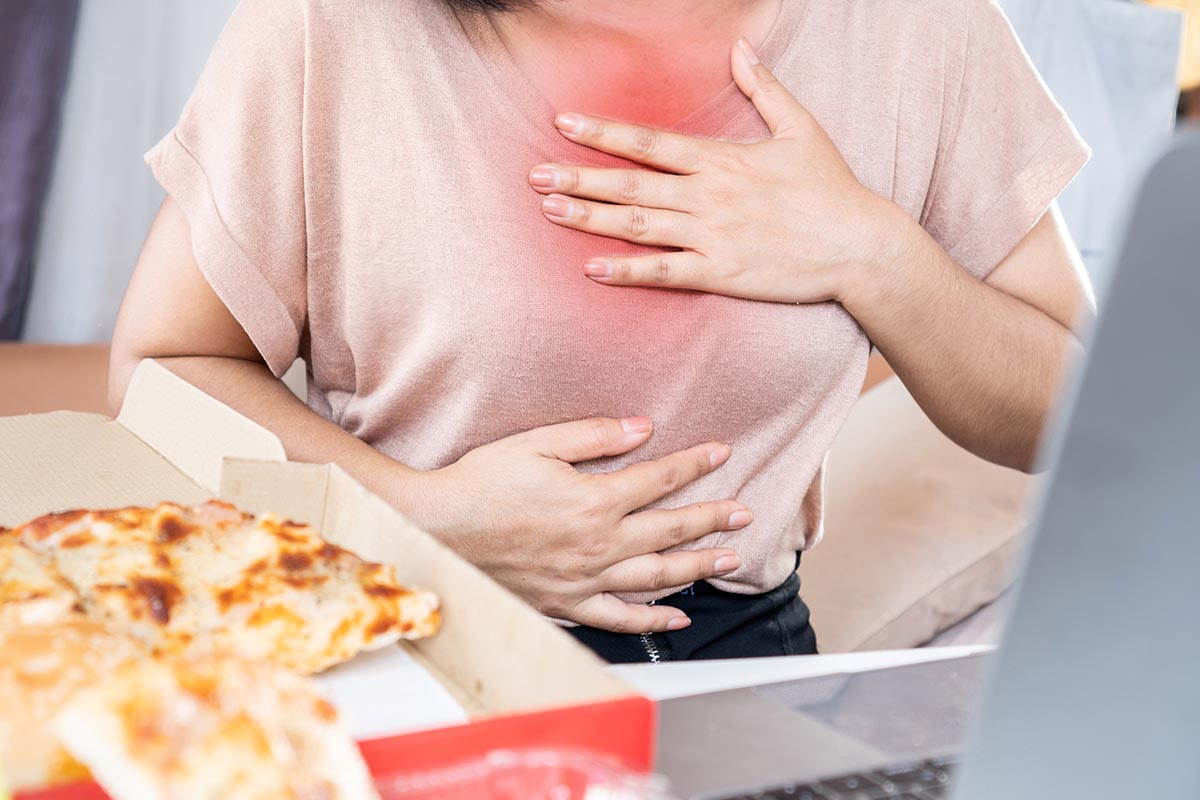 woman-with-heartburn-acid-reflux-holding-her-chest-pizza-in-foreground